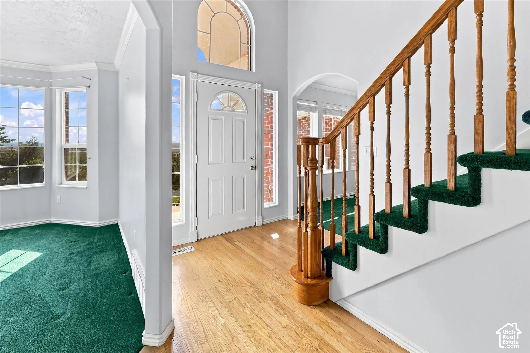 Two-story entryway featuring a hardwood-finish floor, a white paneled door with an arched transom, and a staircase with wood balusters and green carpet treads
