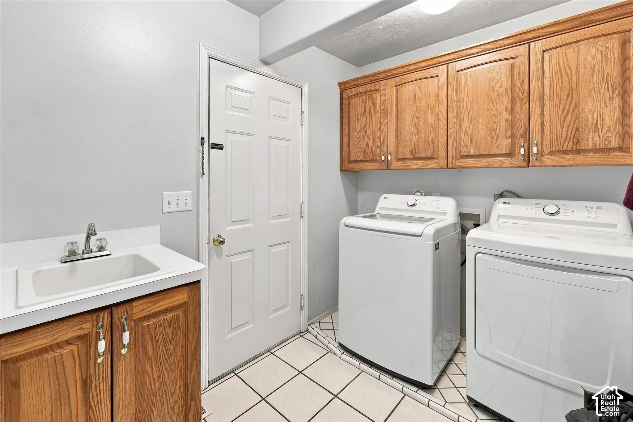 Laundry area featuring a utility sink, wood cabinetry, and white tile flooring