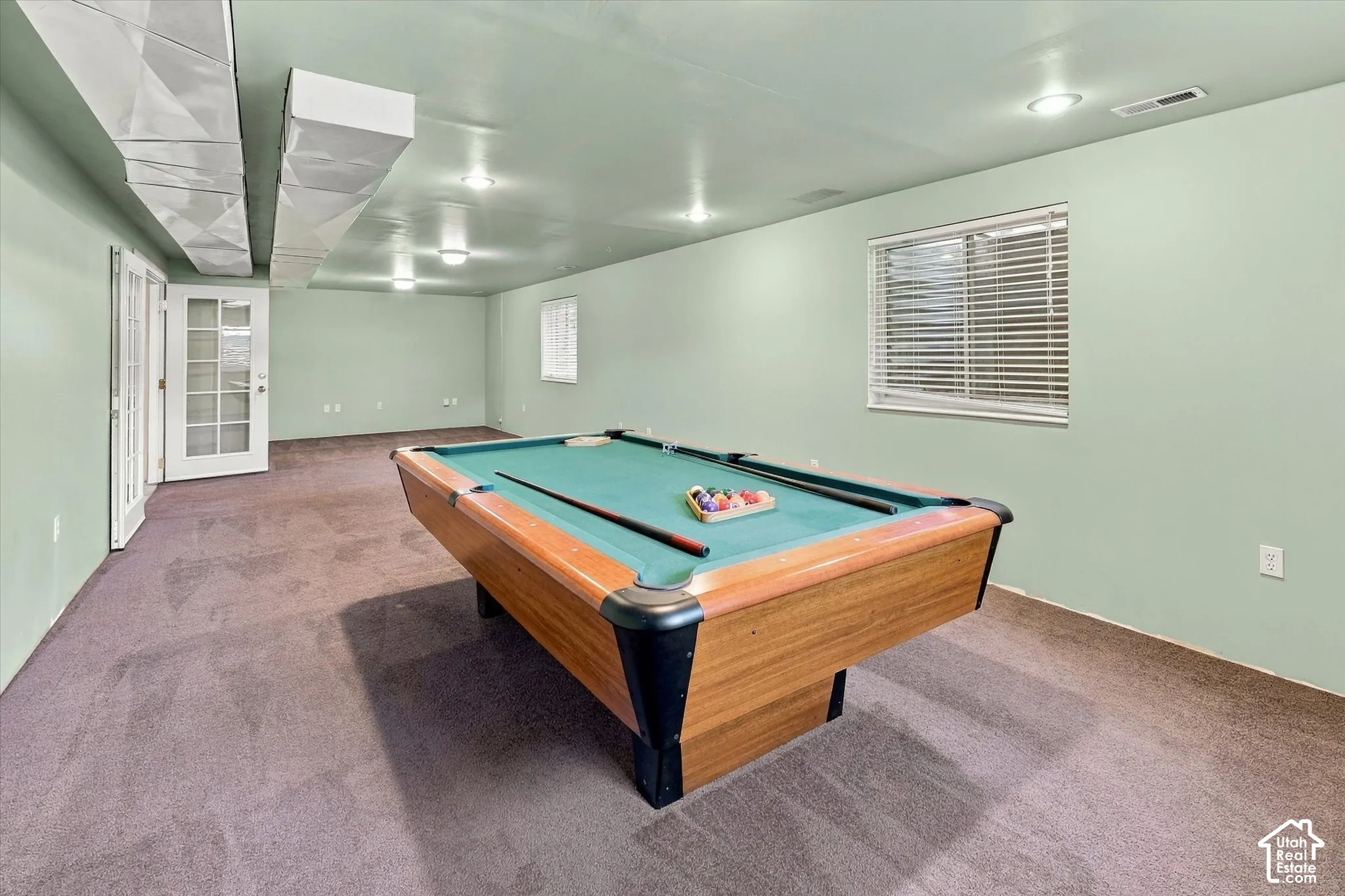 Recessed lighting, exposed ceiling ductwork, dual French doors with glass panes, and a window with blinds. Complete with pool table.