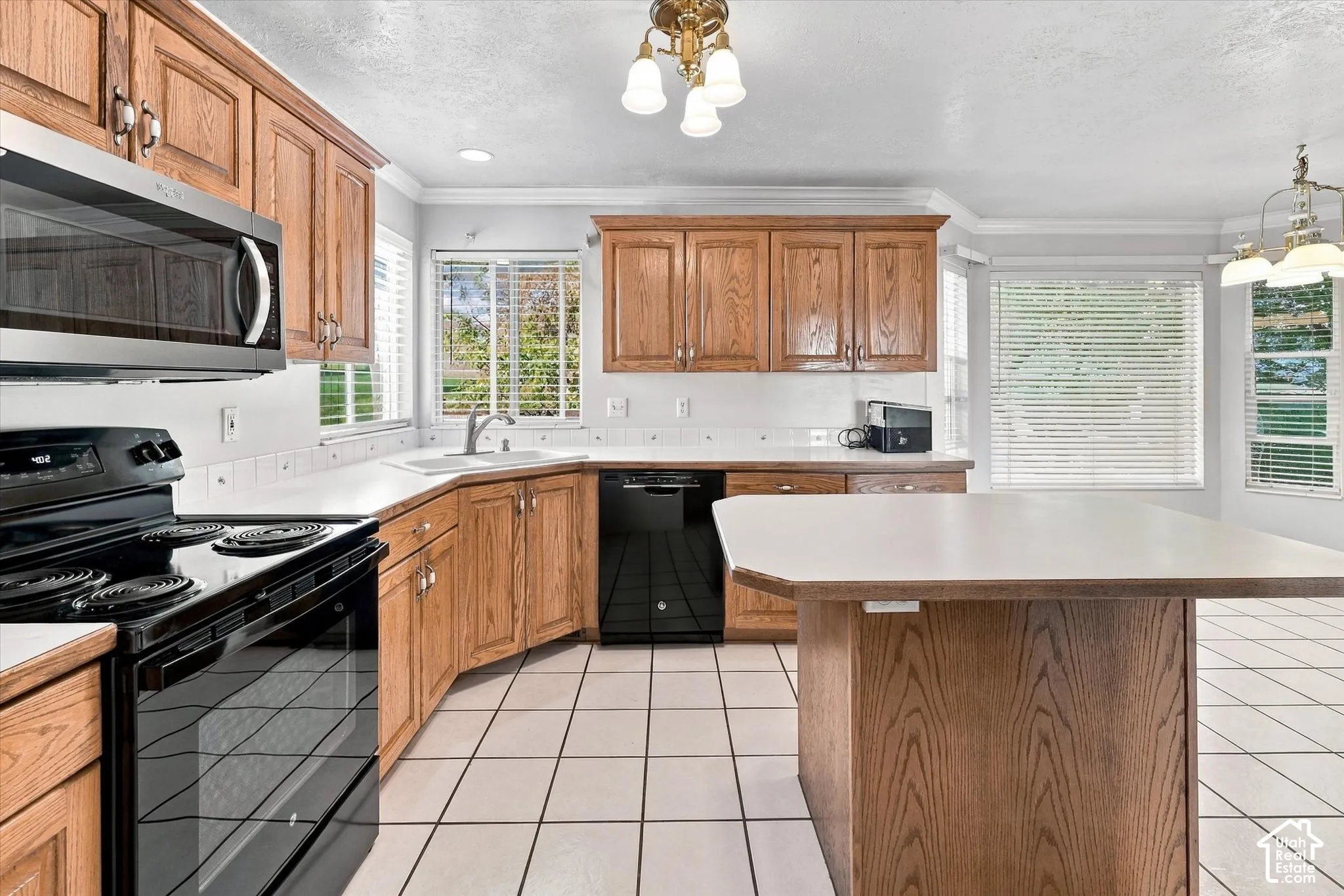 Kitchen featuring wood cabinetry, white countertops, a corner sink with a window, black appliances, and white tile flooring