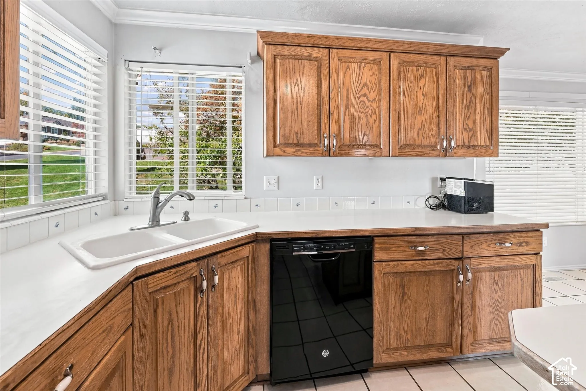 Corner kitchen sink with a double basin, wood-finish cabinetry, and a black dishwasher appliance