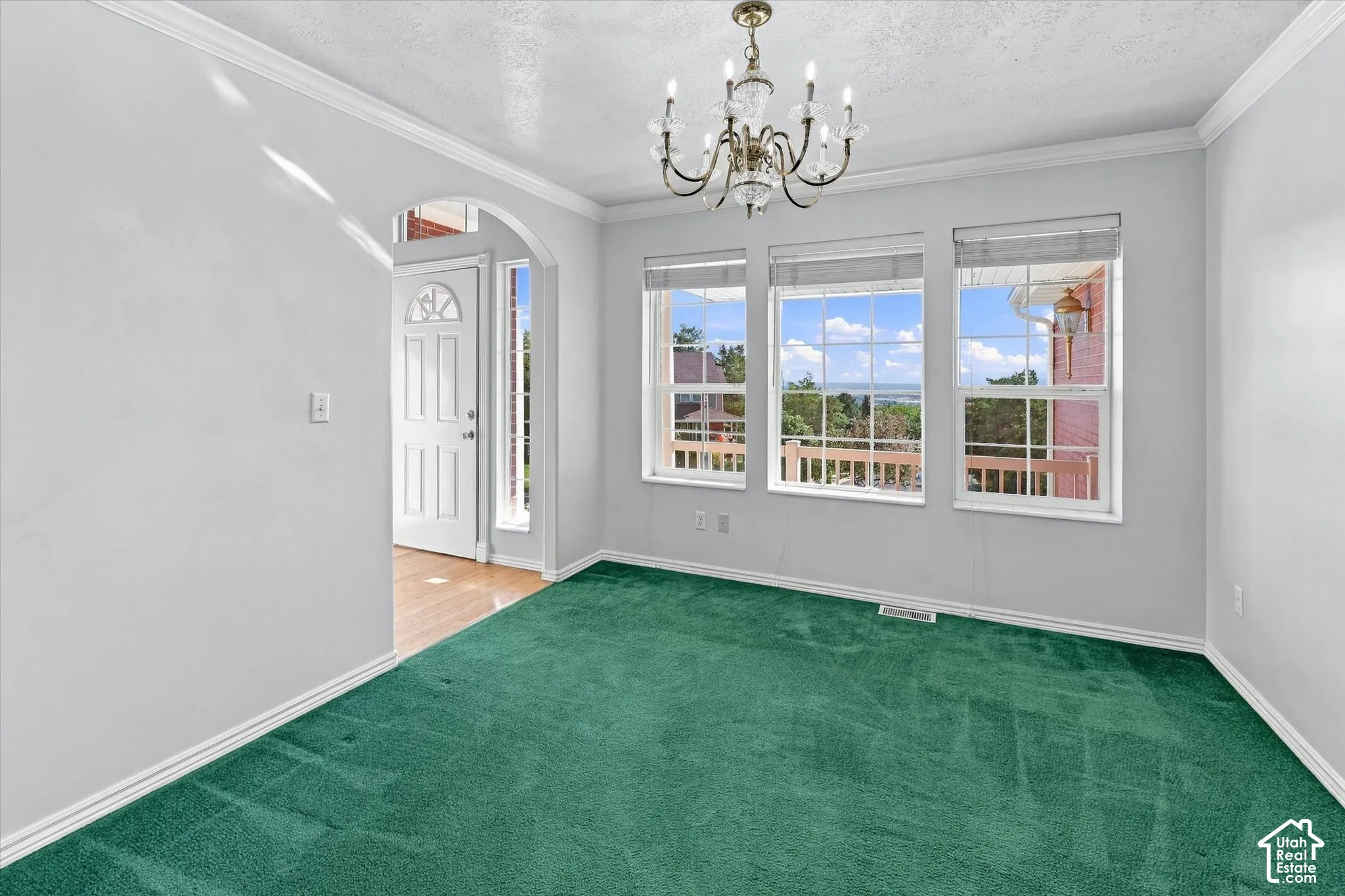 Interior space featuring green carpeting, three windows with blinds, and a decorative chandelier