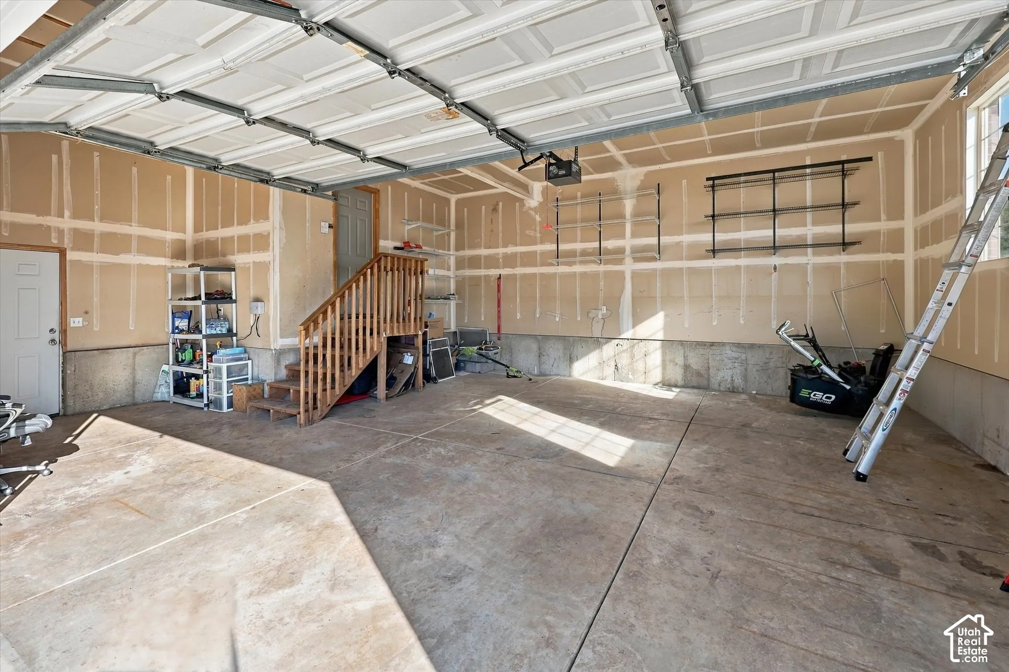 Spacious oversized garage with exposed drywall, concrete flooring, two overhead garage doors, and a wood staircase