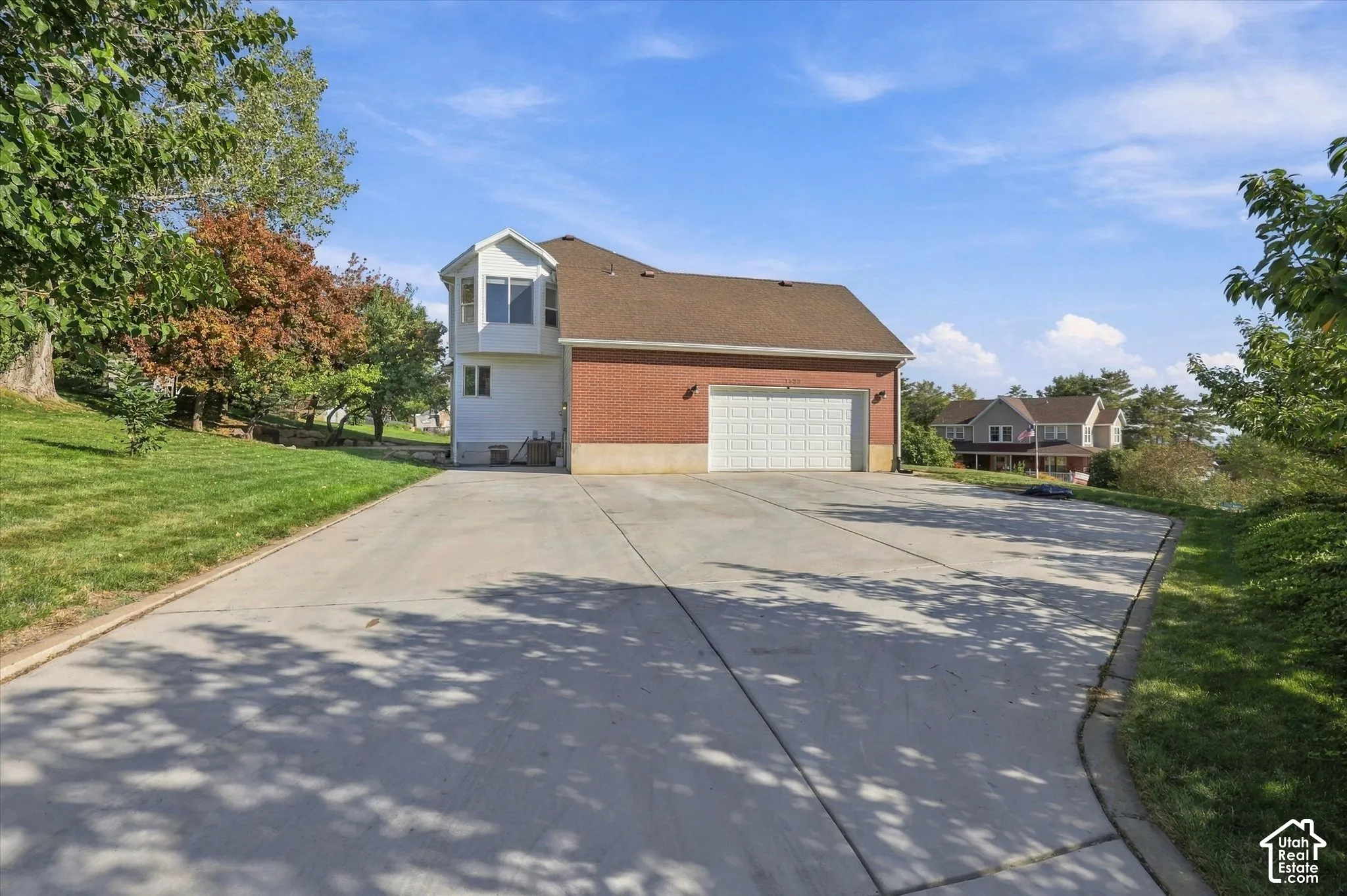 Red brick exterior, multi-panel garage door, bay window, expansive concrete driveway, and established landscaping