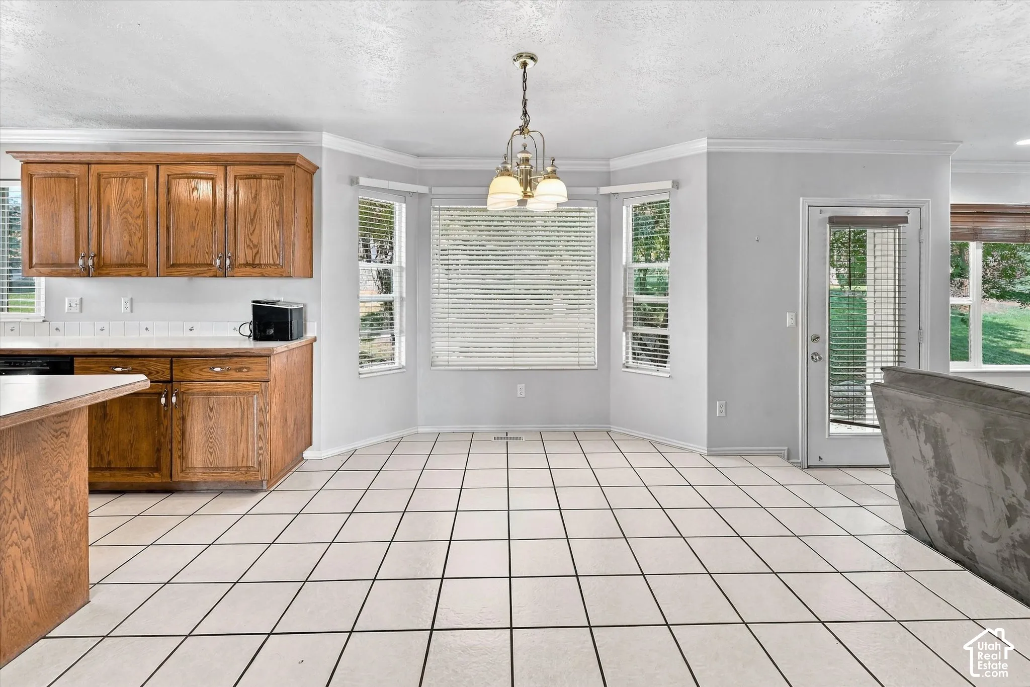 Tile flooring throughout, bay window with multiple panes, wood cabinetry with white countertops, built-in island, and an exterior door with integrated blinds