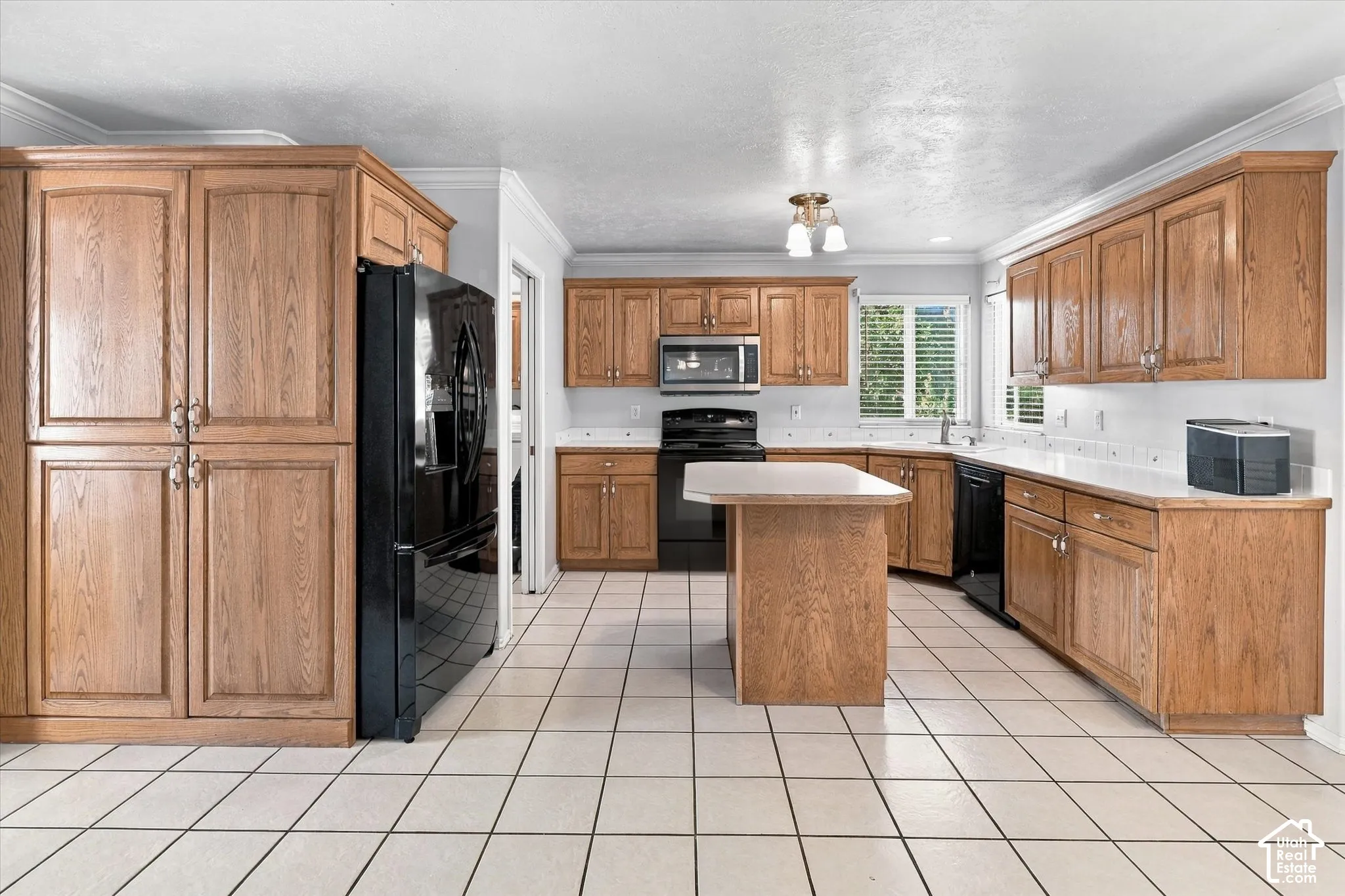 Expansive kitchen featuring light wood cabinetry, white tile flooring, a functional kitchen island, and a full suite of black appliances