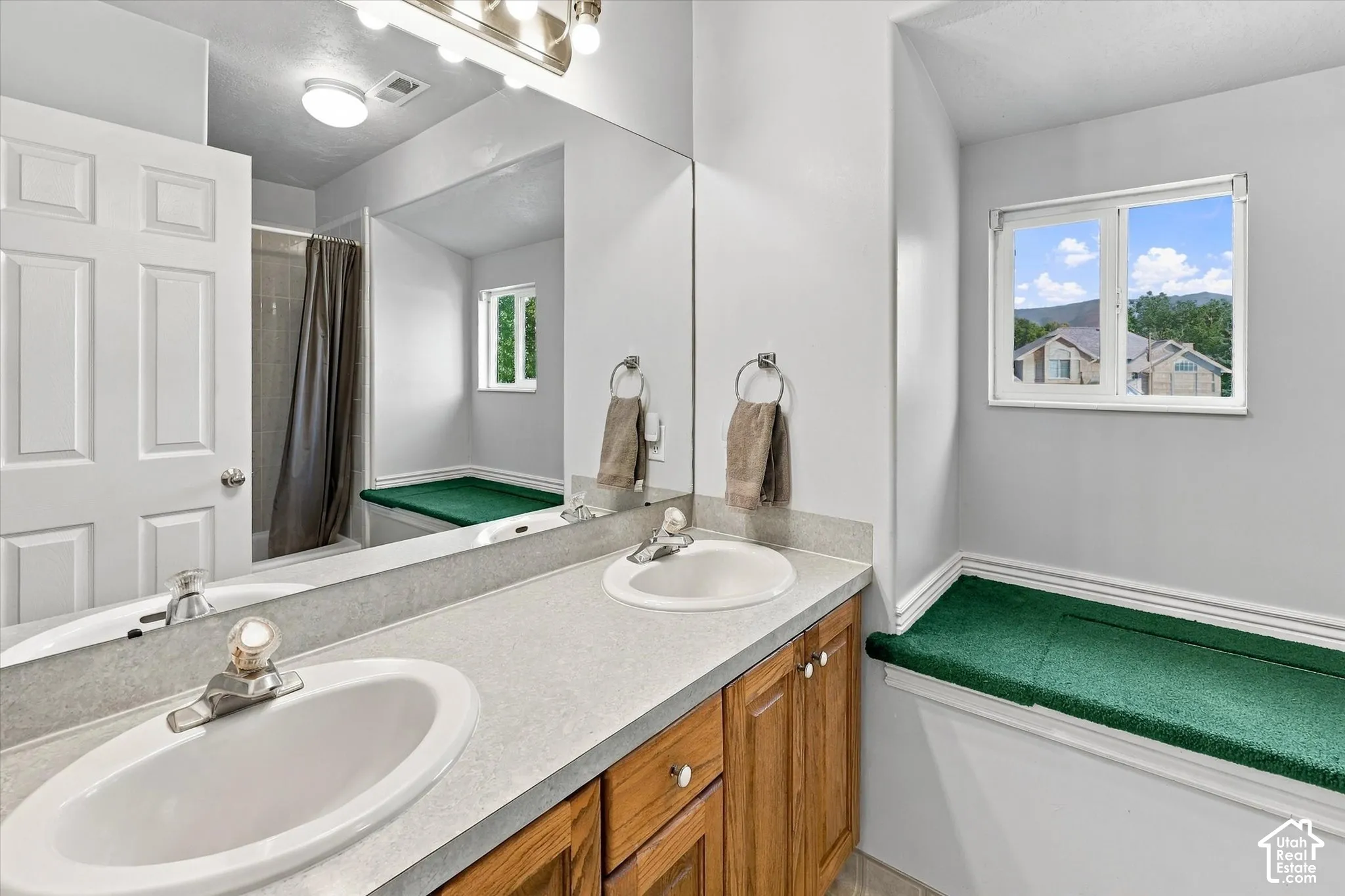 Double vanity with oval sinks, wood-finish cabinetry, and a full-width mirror