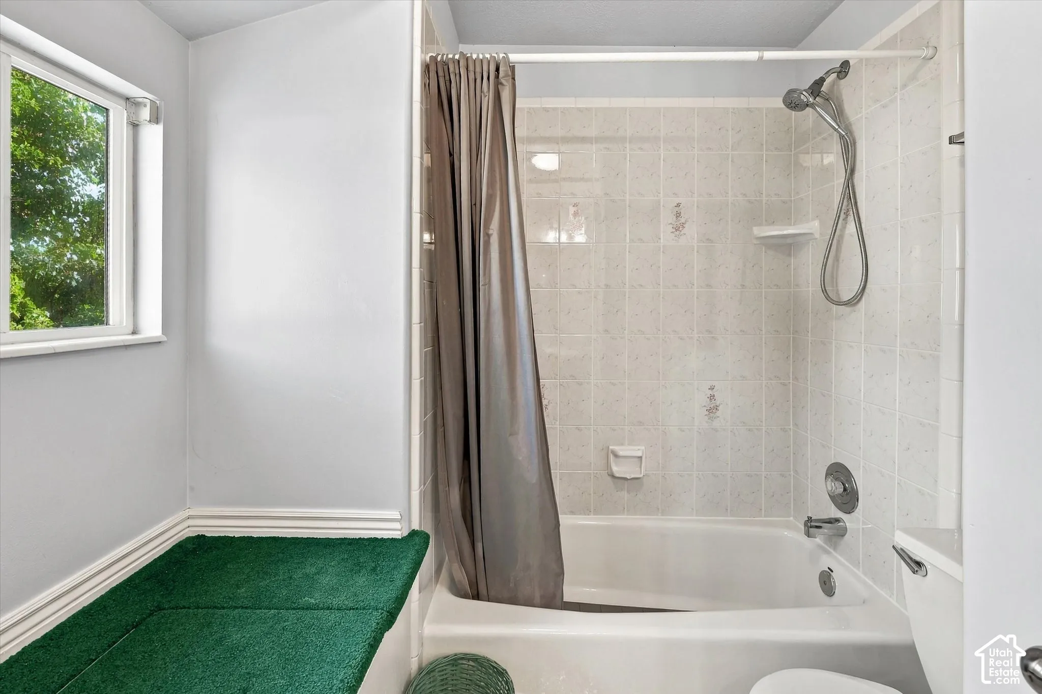 Bathtub with tiled surround, shower fixture, and a window with natural light