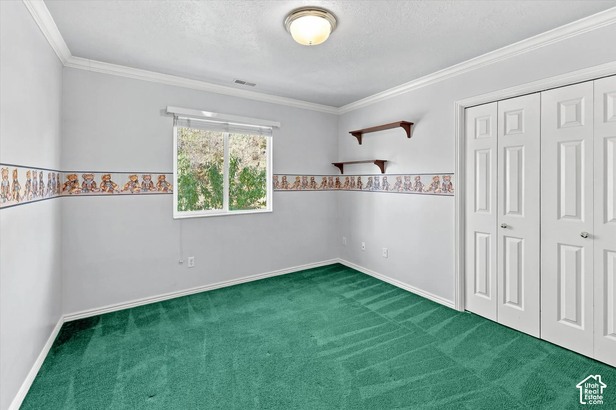 Wall-to-wall green carpeting, white bi-fold closet doors, crown molding, and a flush mount ceiling light fixture