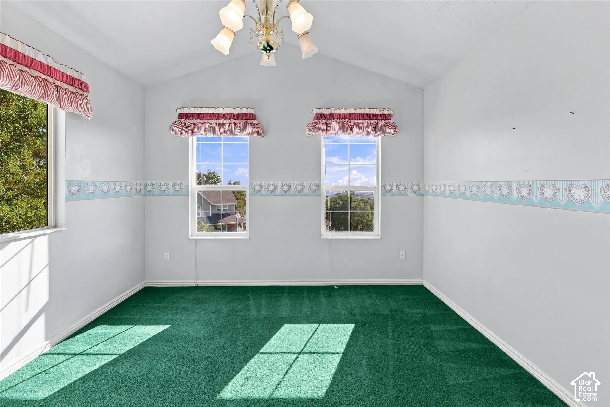 Vaulted ceiling, ceiling-mounted light fixture, three windows, green carpet flooring, decorative wall border