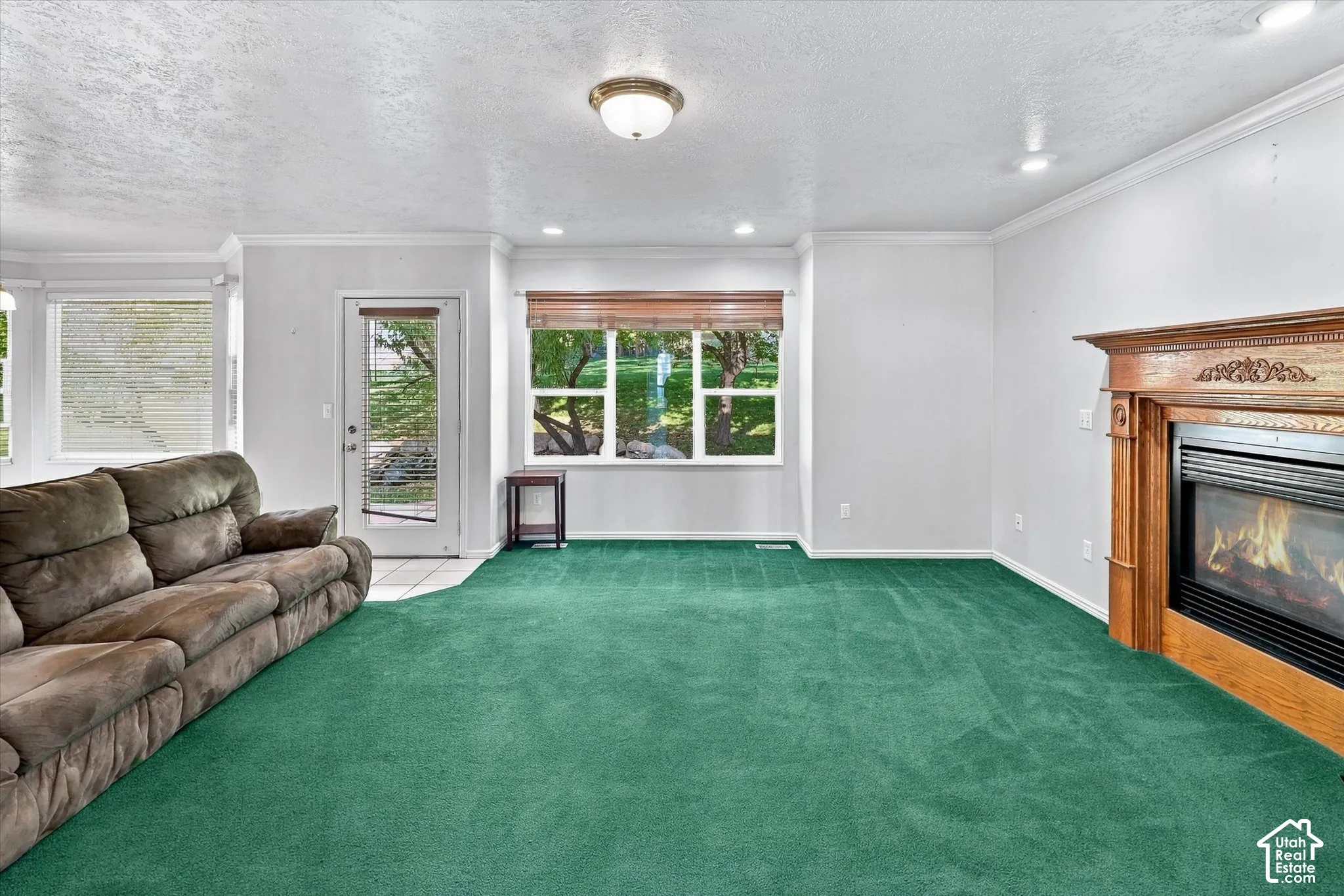 Spacious room with plush green carpeting, a decorative wood-mantle fireplace, and recessed lighting