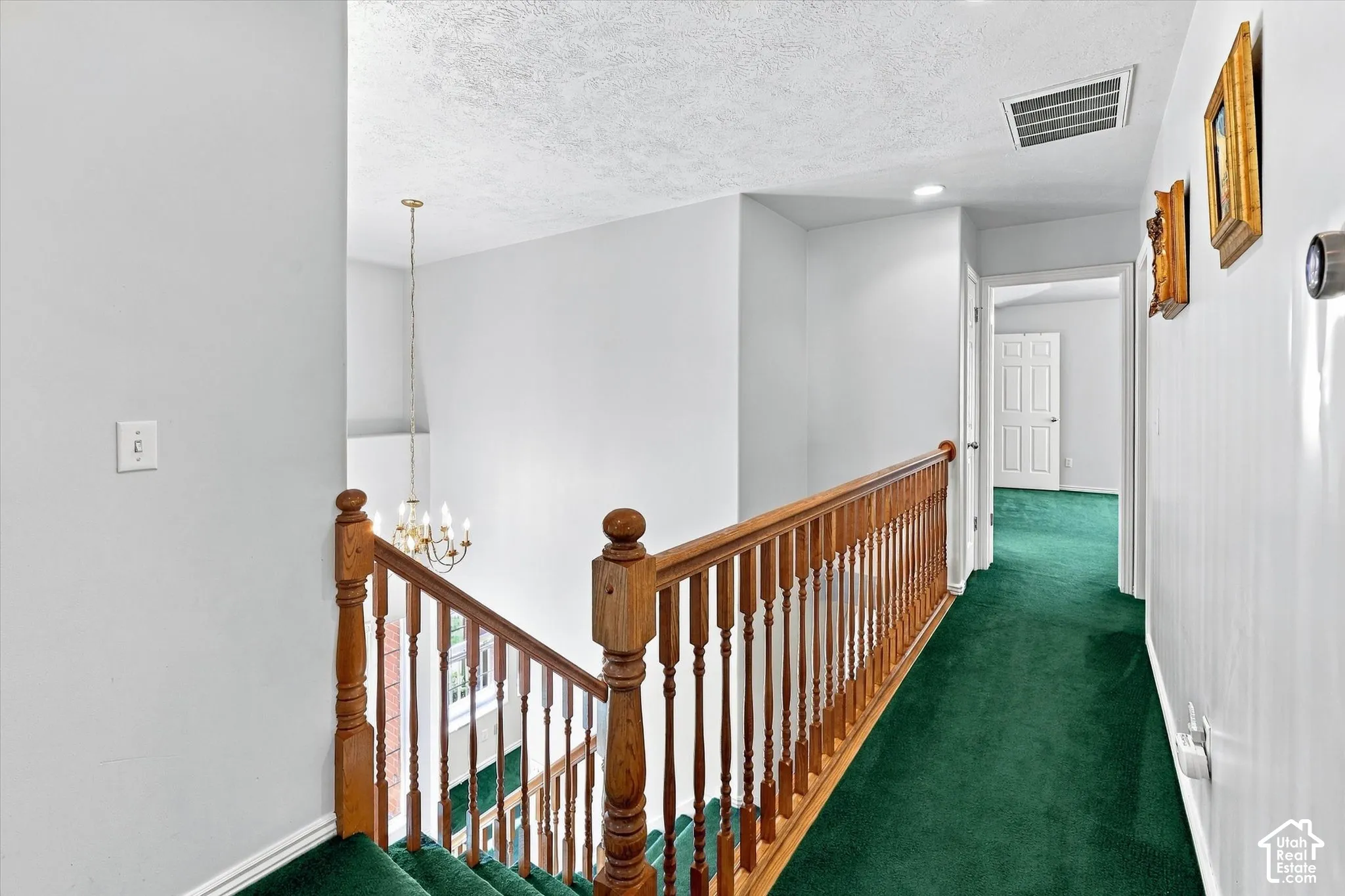 Staircase with wood banister and spindles, green carpeted flooring, and white painted walls