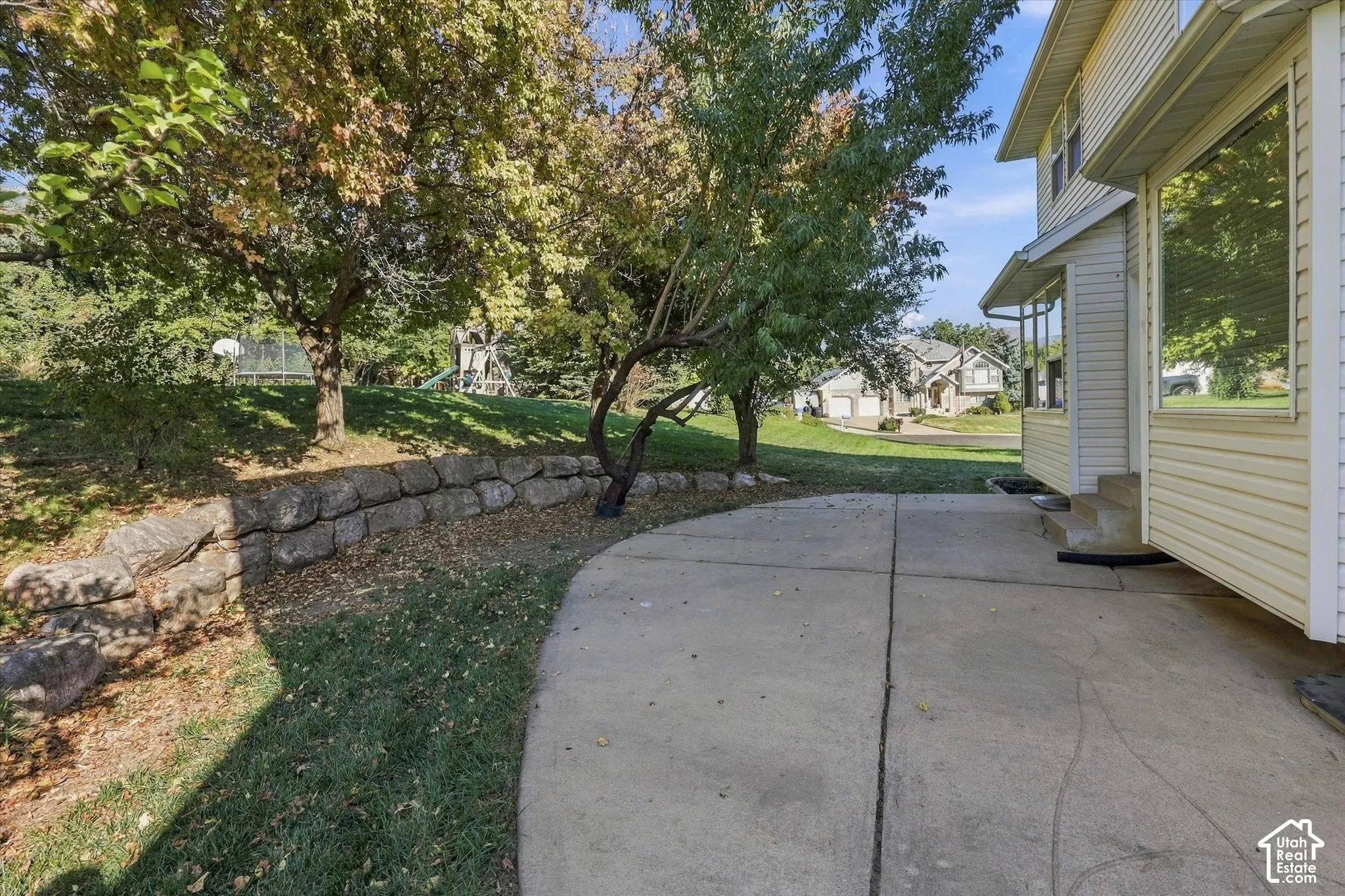 Backyard, concrete pathway with a stone retaining wall and mature trees
