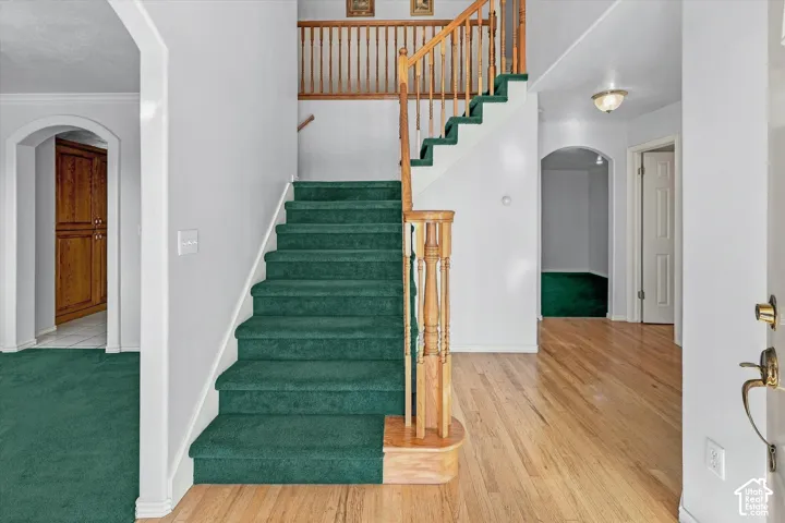 Wood-finish flooring, staircase with wood banister and green carpeting, white trim throughout, and arched doorways