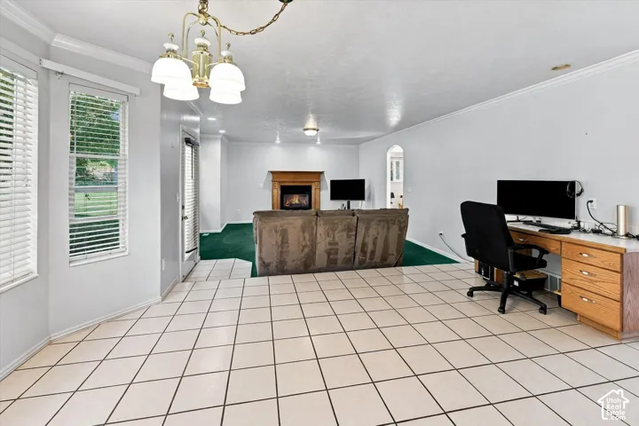 Expansive tiled flooring, a built-in desk, multiple windows, a decorative chandelier, and a fireplace with a wood mantle