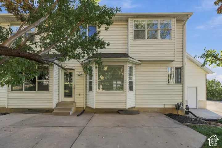 Exterior featuring light-toned horizontal siding, a bay window, concrete patio, and mature trees