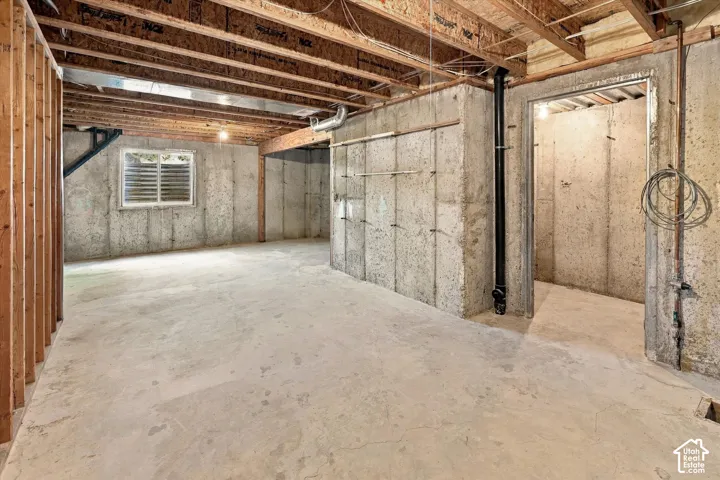 Unfinished basement featuring exposed wood joists, concrete foundation walls, a single window with horizontal blinds, and a concrete floor