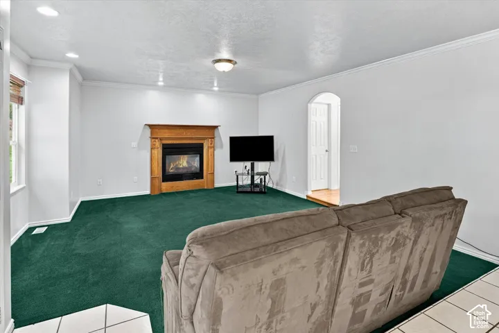 Recessed ceiling lighting, crown molding, fireplace with wood mantel, arched doorway, and a window with blinds