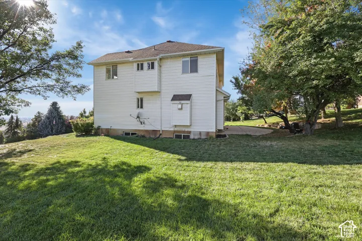 Large side yard on cul-de-sac. White multi-level property with a brown shingle roof, surrounded by mature trees and a sloped lawn