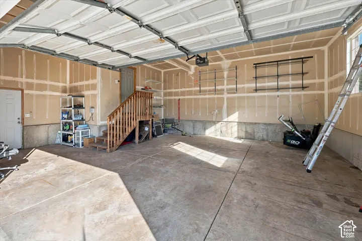 Spacious oversized garage with exposed drywall, concrete flooring, two overhead garage doors, and a wood staircase