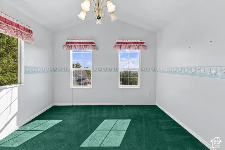 Vaulted ceiling with a central chandelier, green carpeting, and multiple windows