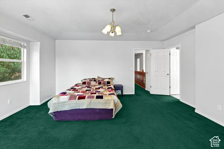 Spacious room featuring broadloom carpeting, crisp white walls, a large window, a three-light chandelier, and a paneled door