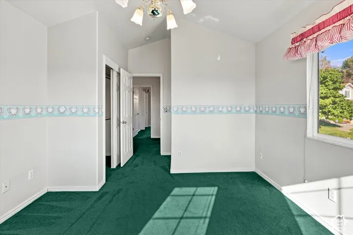 Vaulted ceiling, green carpeting, white baseboards, white walls, and a window with exterior views