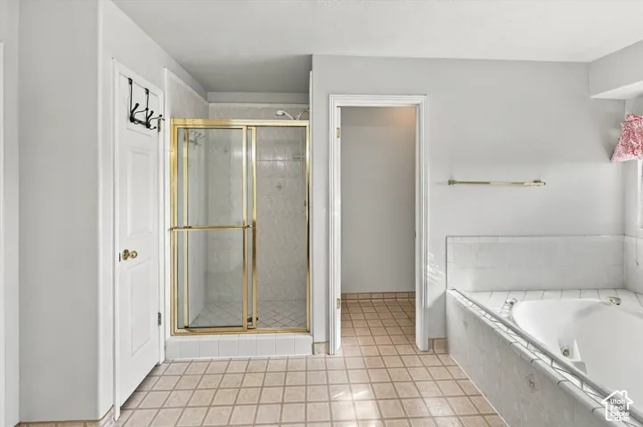 Recessed tub with tiled surround, separate shower with brass-finish sliding glass enclosure, and neutral square tile flooring