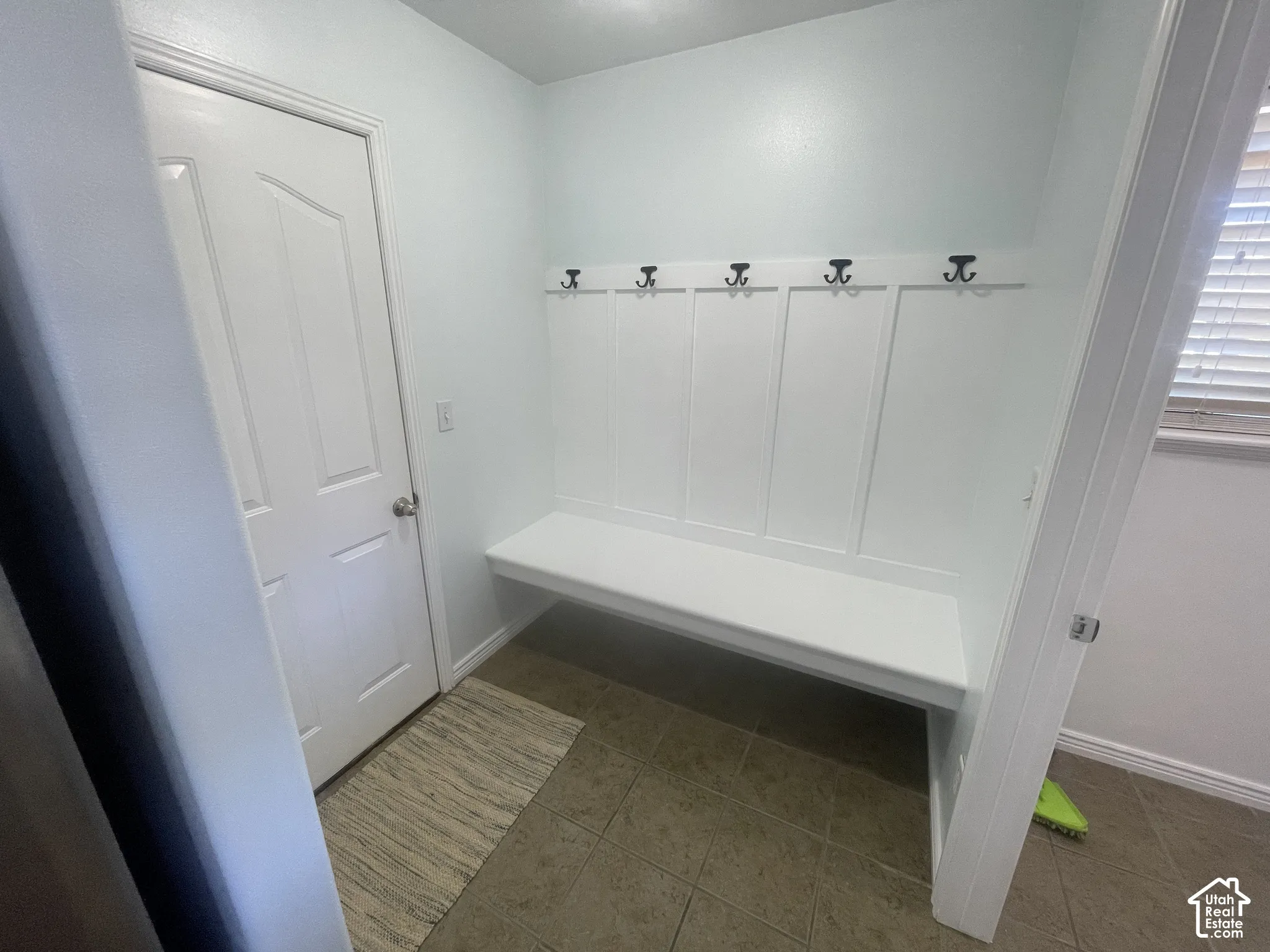 Built-in bench with integrated coat hooks, paneled wainscoting, and tile flooring