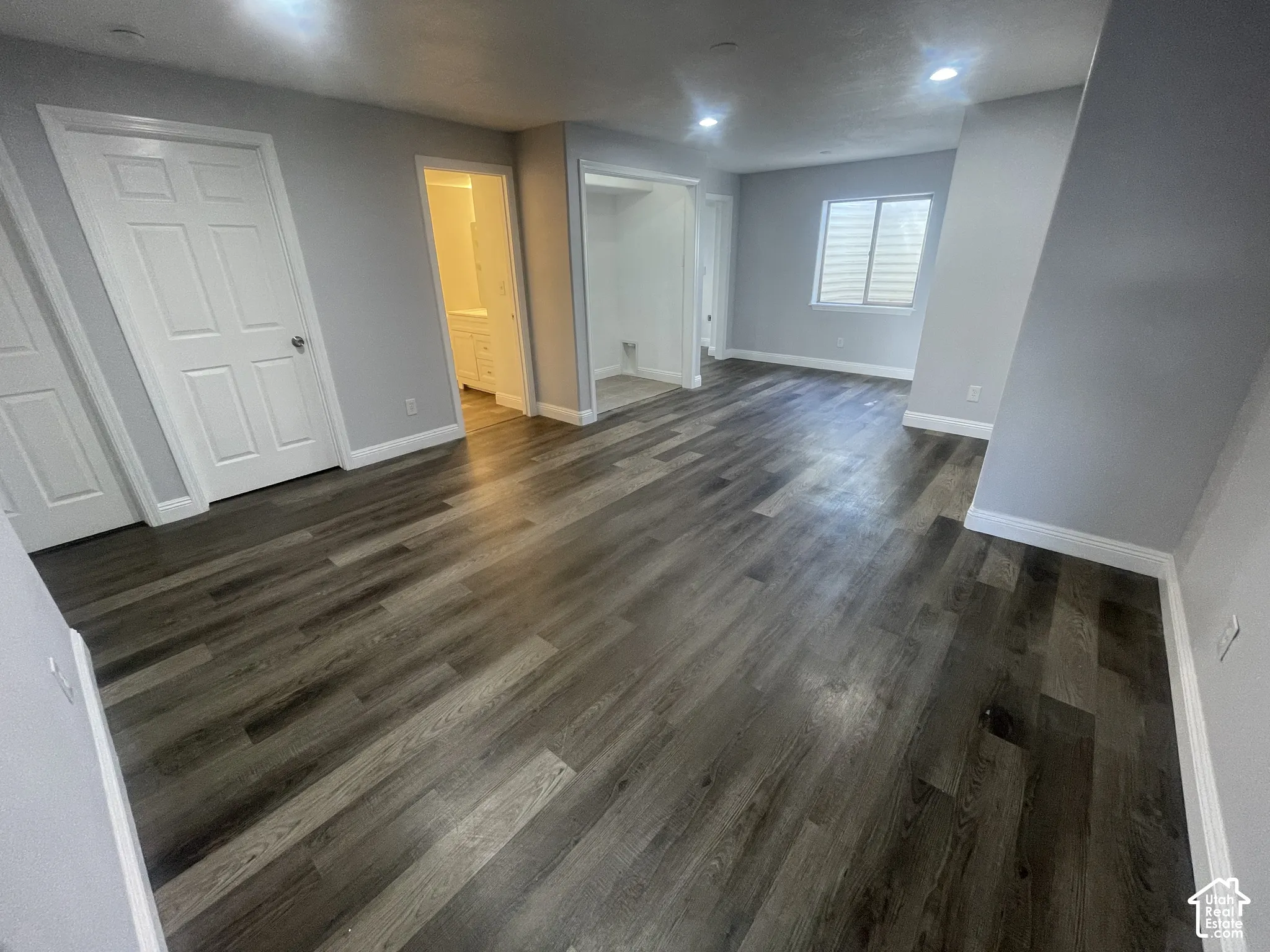 Wood-finish flooring throughout, light gray wall paint, recessed lighting, white baseboards, and a window with horizontal blinds