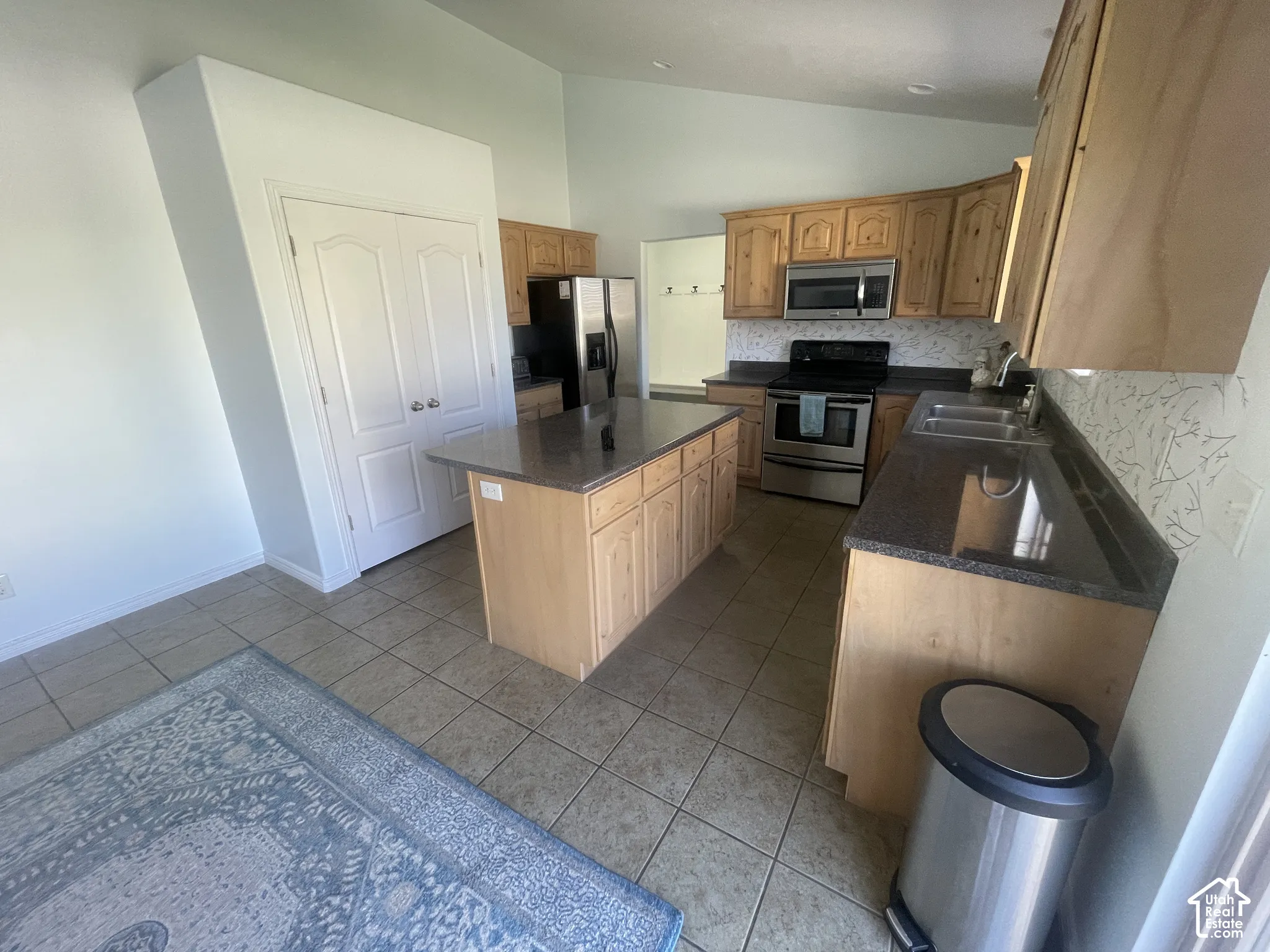 Kitchen featuring light wood cabinetry, a central island, dark countertops, tile flooring, and stainless steel appliances