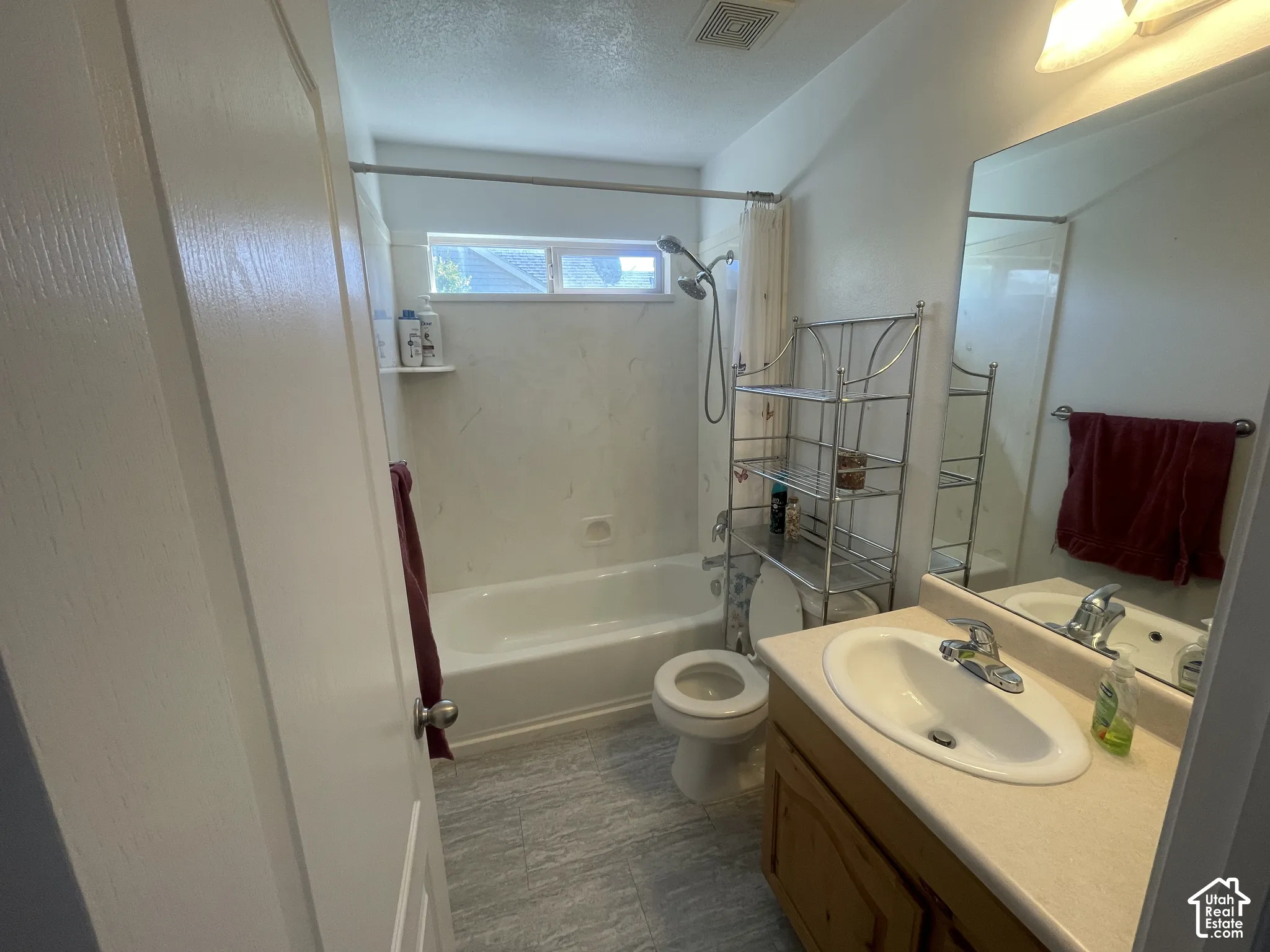 Bathroom featuring a built-in bathtub with shower, a single vanity with an integrated sink, a large wall-mounted mirror, and tile flooring