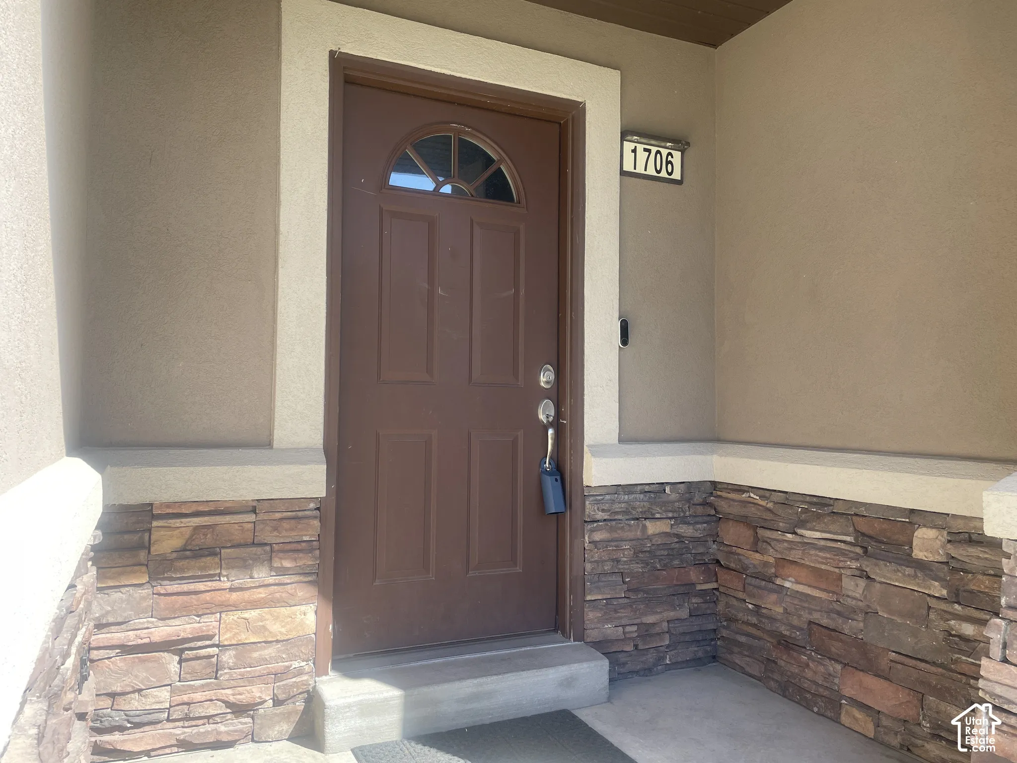 Entryway featuring a brown panel door with an arched window insert, stucco siding, and stacked stone accents
