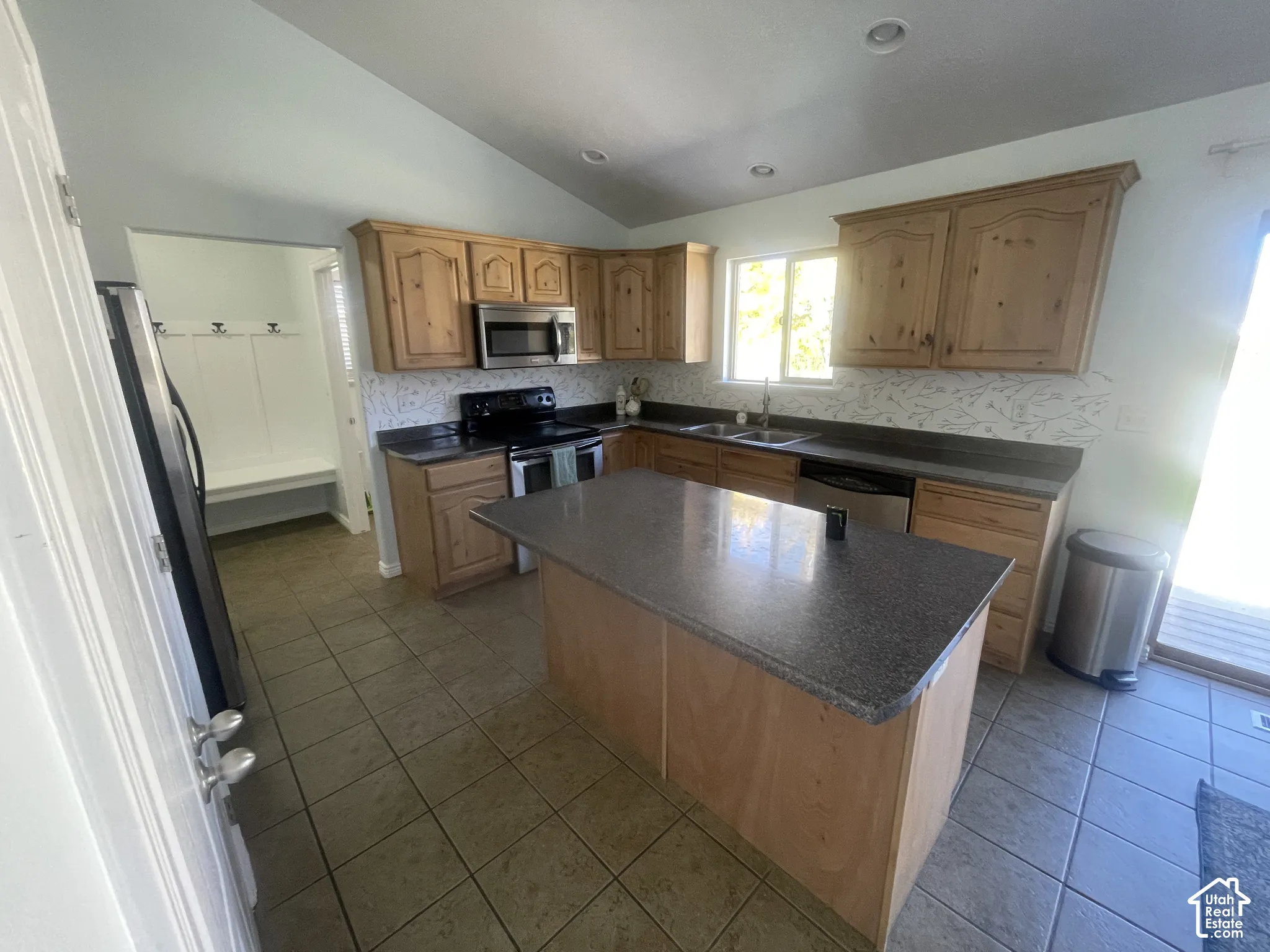 Kitchen featuring wood cabinetry, speckled countertops, stainless steel appliances, and a central island