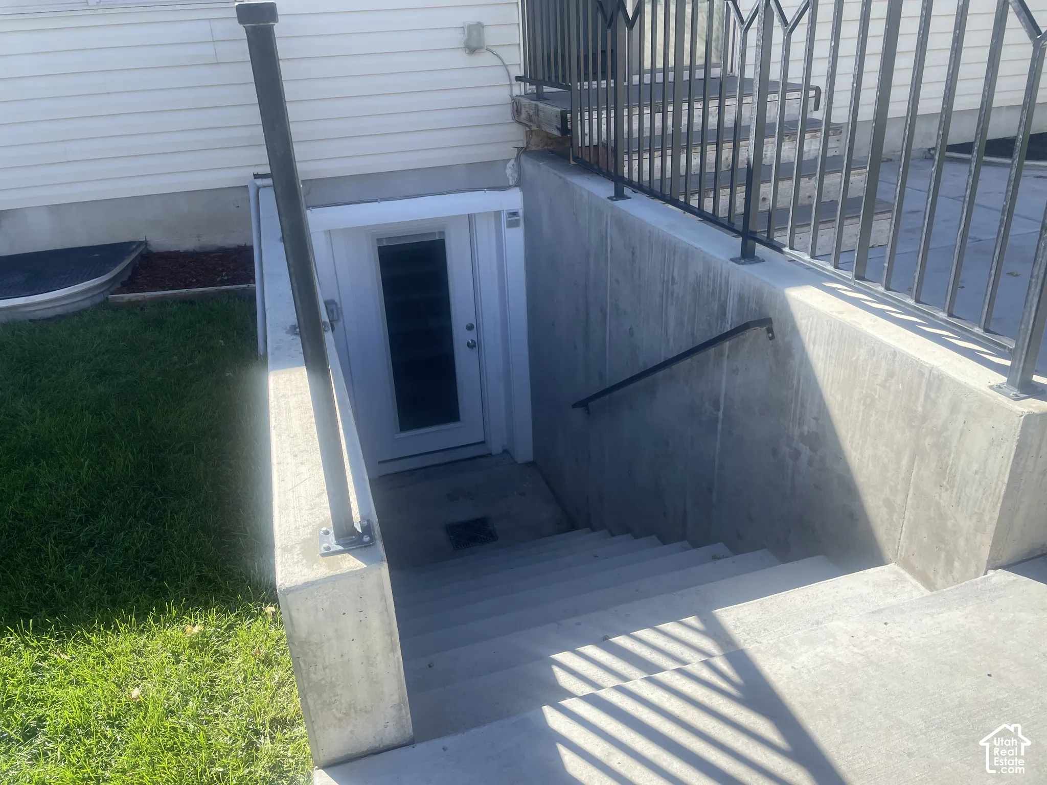 Concrete exterior stairwell with a white door, black metal handrails, and a wrought iron railing