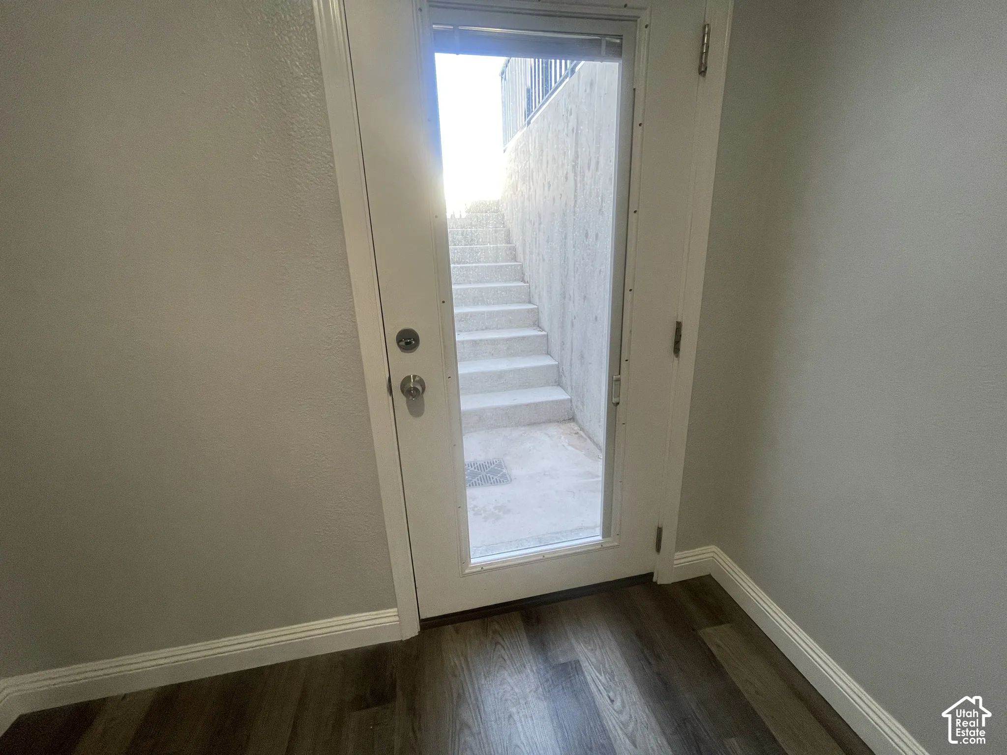 Wood-finish flooring with white baseboards, a white door with a clear glass insert, and concrete exterior stairs