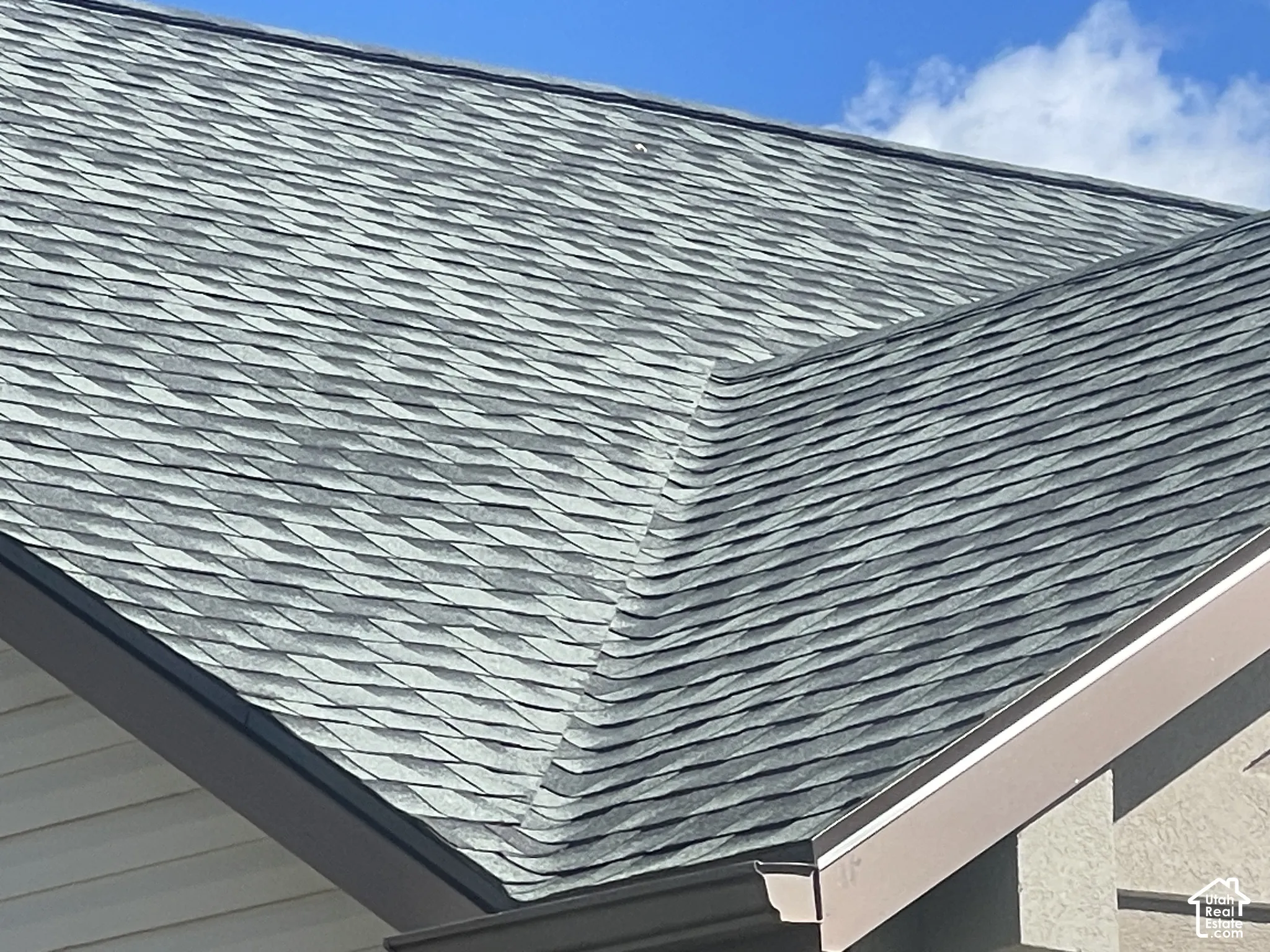 Architectural asphalt shingle roof featuring a distinctive layered design in slate blue-gray tones with clean lines and professional installation visible along the peak and eave transitions