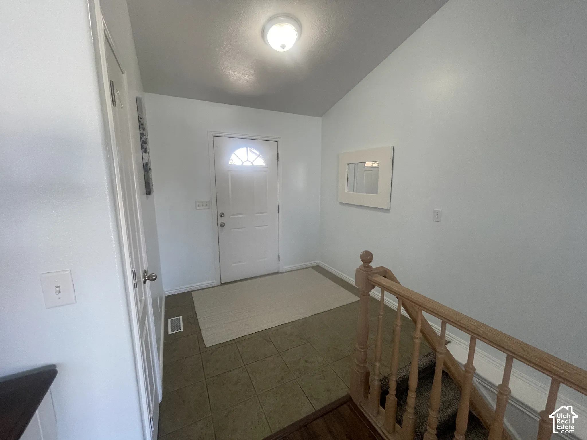 Entryway featuring a white paneled door with an arched window, tile flooring, and a light wood-finish staircase railing
