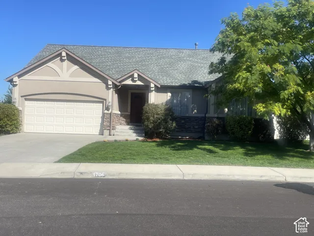 Stucco and stone facade with a paneled garage door, a shingled roof, a paved driveway, and a manicured lawn