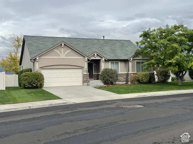 Stucco exterior with stone accents, attached two-car garage, concrete driveway, lush lawn, and mature landscaping