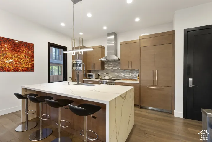 Gourmet kitchen featuring a waterfall island, integrated appliances, wood-finish cabinetry, a tile backsplash, and recessed lighting
