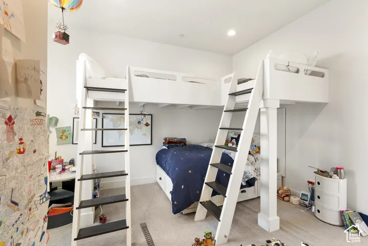 Bright, dual loft-style bedroom featuring built-in bunk beds with integrated storage shelving, wood-finish flooring, recessed ceiling lighting, and ample natural light from multiple windows