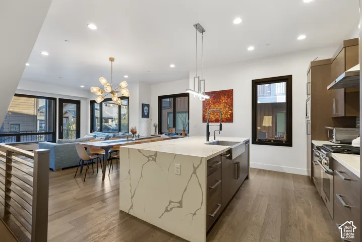 Contemporary kitchen and dining space showcasing a large center island with quartz countertop, stainless steel appliances, custom cabinetry with horizontal slat detailing, recessed and pendant lighting, wide-plank wood-finish flooring, and expansive windo
