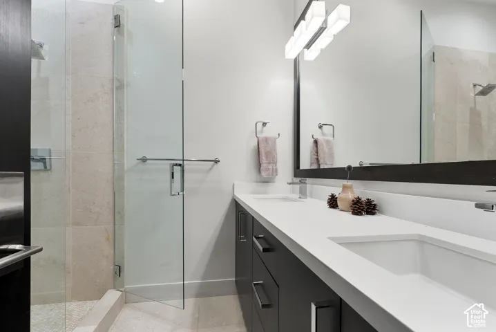 Dual vanity with integrated rectangular sinks and white countertops, framed mirror with horizontal lighting fixture, and a glass-enclosed shower with tile surround and pebbled floor