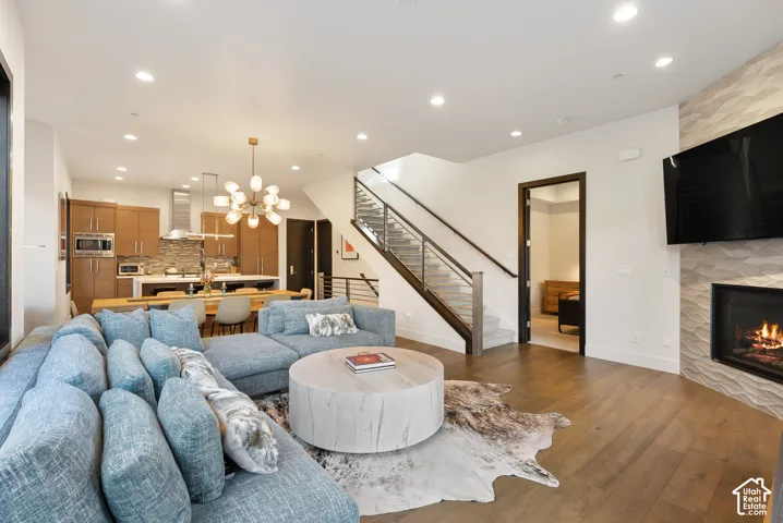 Open concept living space with wood-finish flooring, a modern fireplace with a textured surround, and a contemporary staircase with a glass railing