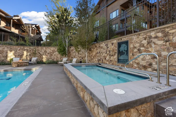 Community swimming pool with an integrated spa, stone retaining wall, and a stone fire pit area
