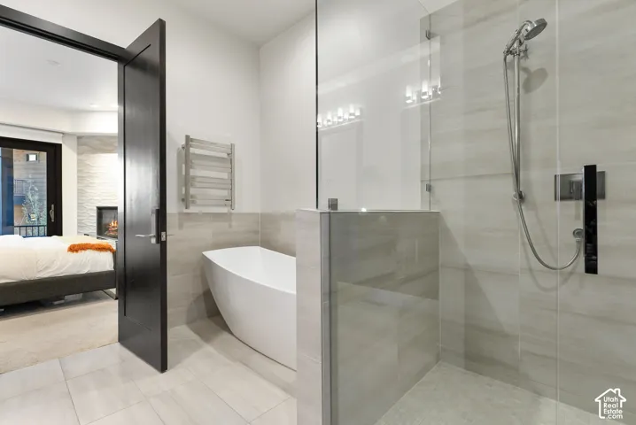 Spa-inspired primary bathroom featuring a freestanding soaking tub, walk-in shower with frameless glass enclosure and rainfall showerhead, heated towel rack, dual pendant lighting, and light stone-finish flooring throughout