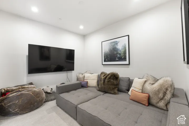 Media Room featuring a wall-mounted flat-screen television, modular gray upholstered seating with quilted detailing, recessed ceiling lighting, light wood-finish flooring, and framed wall art