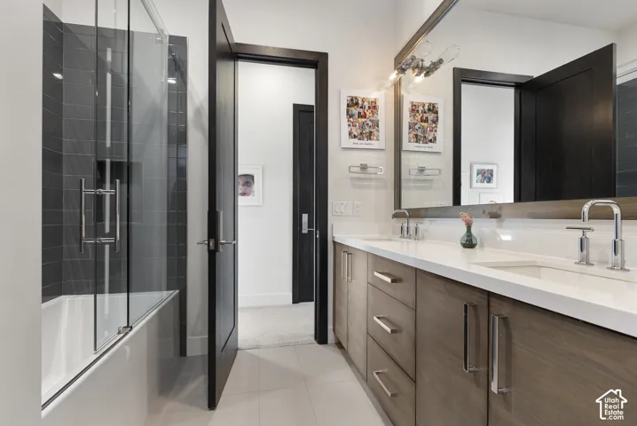 Dual vanity with integrated sinks, wood-finish cabinetry, frameless glass shower enclosure, dark tile tub surround, and polished chrome fixtures