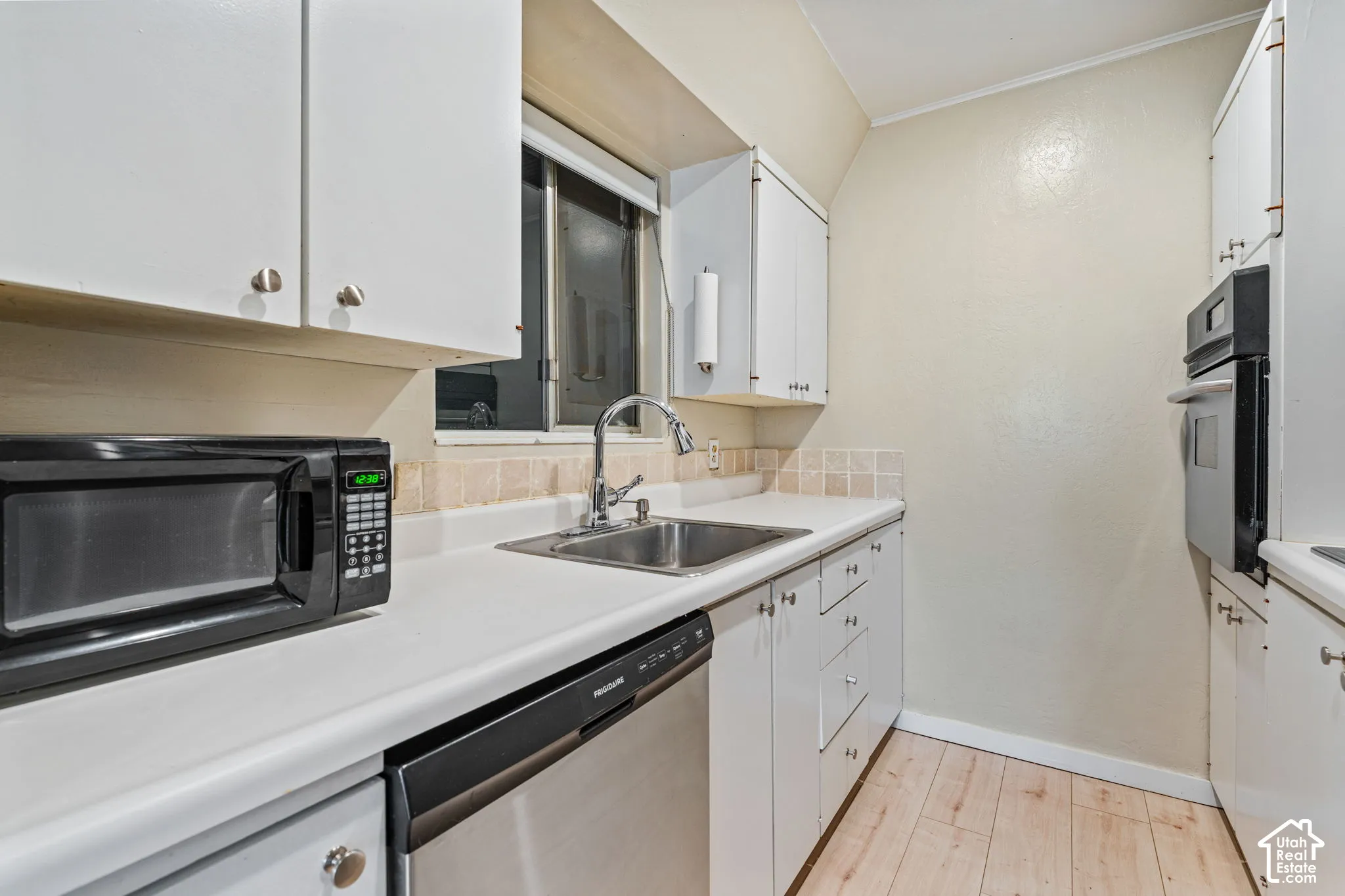 White cabinetry with silver-tone hardware, a stainless steel sink with a chrome faucet, and a built-in wall oven
